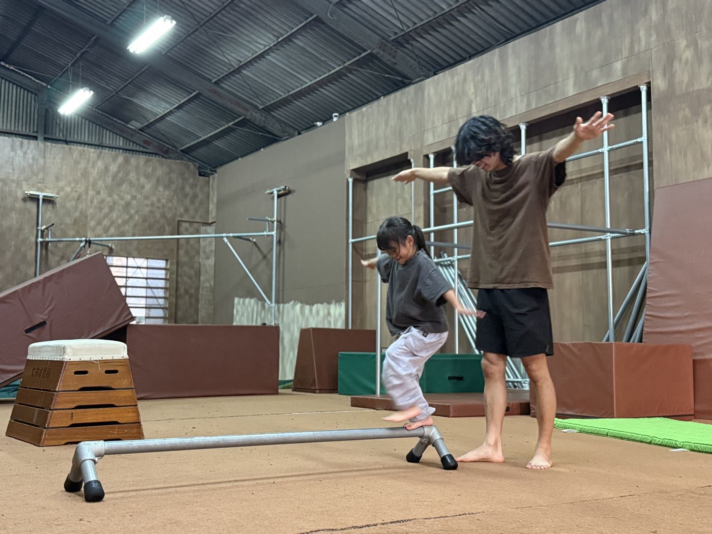 低いレールの上をバランスを取って歩く子どもと、両手を広げて見せるコーチ