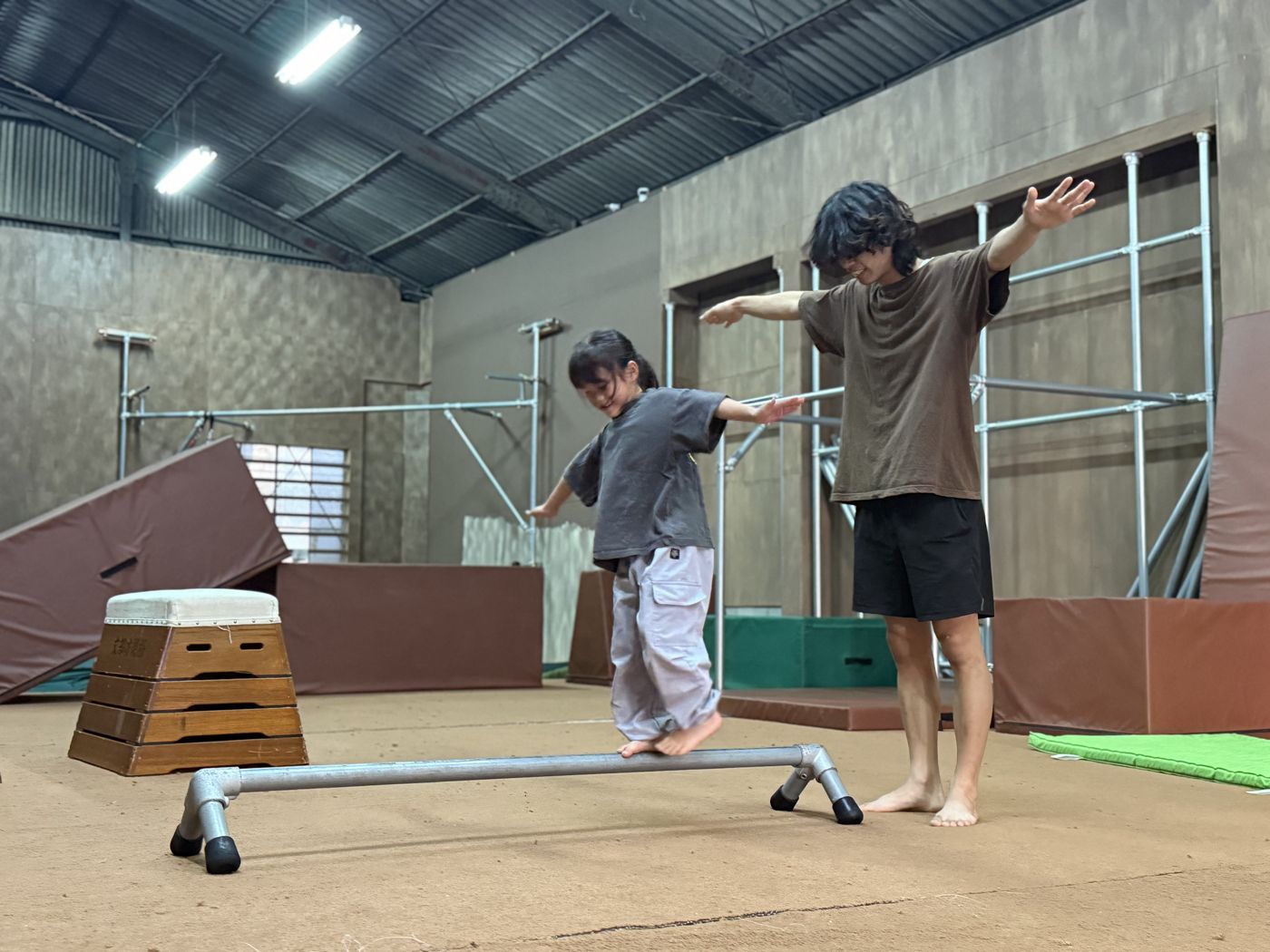 低いレールの上でバランスを取る子どもを、コーチが両手を広げて見守る