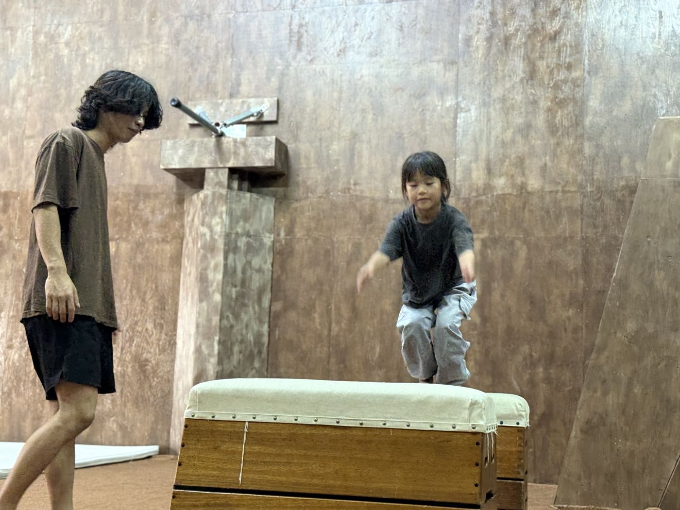 跳び箱から跳び降りて着地する子どもを、横で見守るコーチ