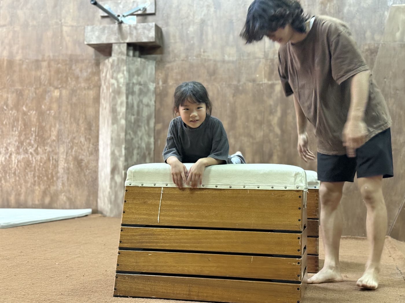 跳び箱の上に手をついて笑う子どもと、横で見守るコーチ