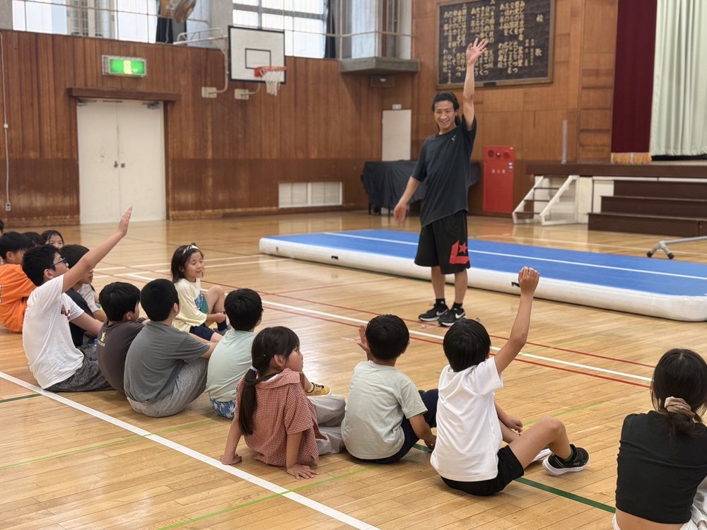 小学校の体育館で子どもたちを前に話すPK Guildのコーチ