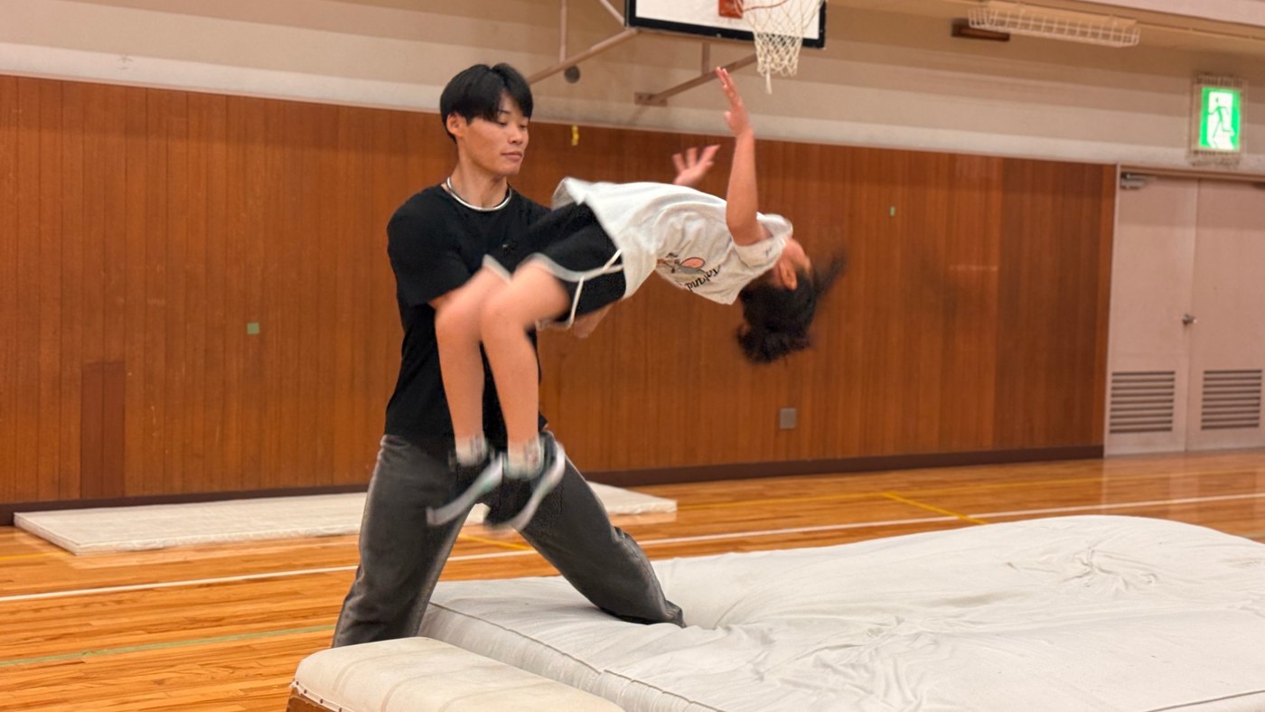 体育館のマットで、指導者が子どもの回転動作を補助している様子